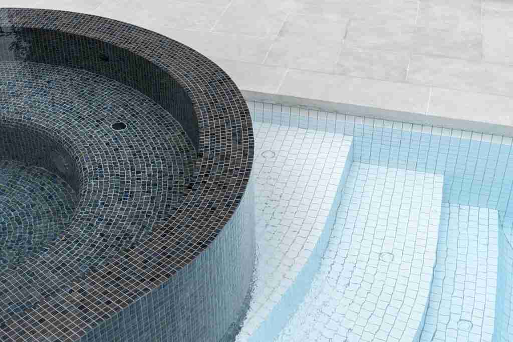 The edge of a rounded Laguna spa with Bisazza black Tripoli tile and white ceramic tiles in the pool by the Pool Tile company